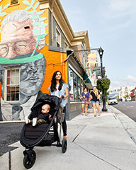 mother walking down a sidewalk with her baby in a stroller with a mural in the background